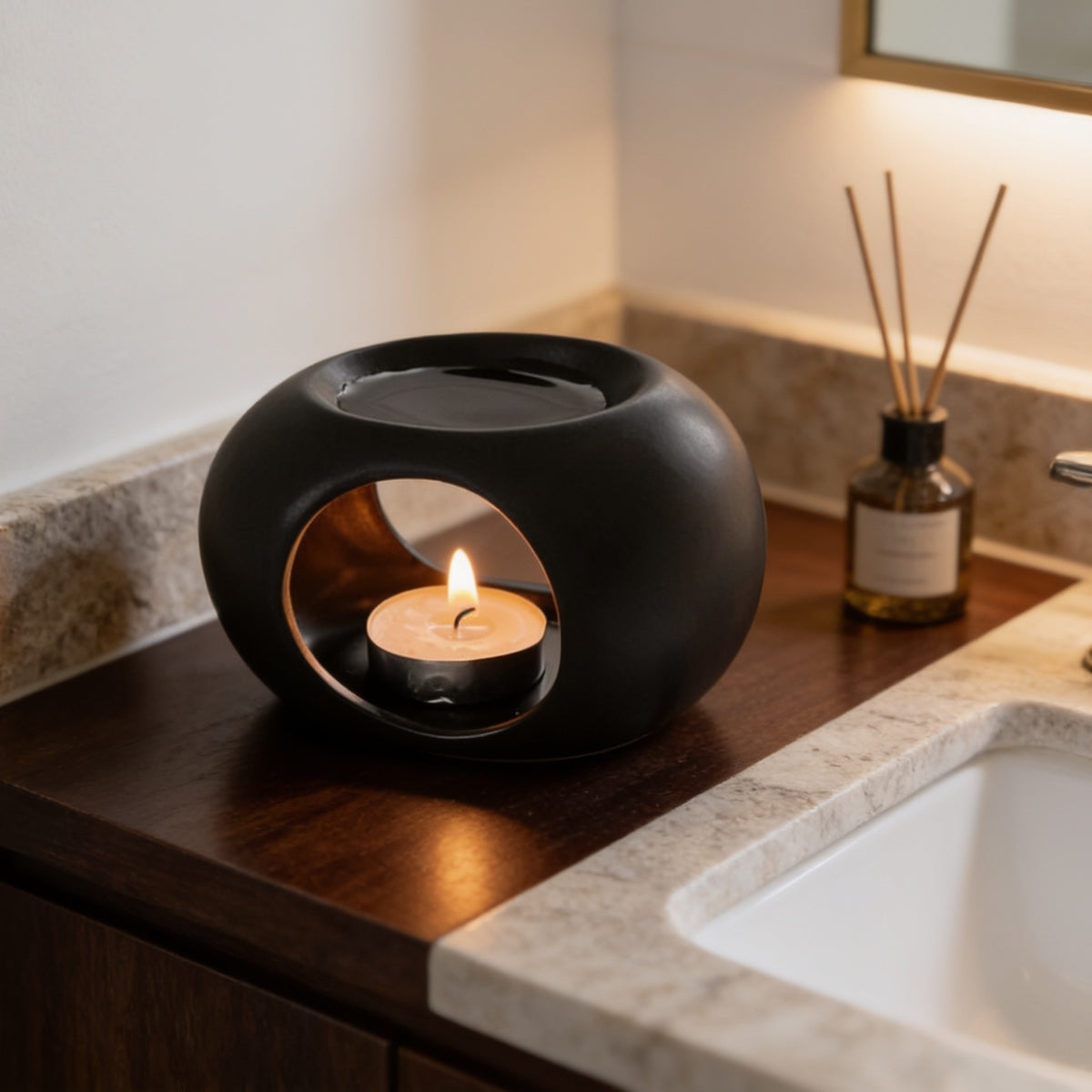 Matte black ceramic warmer with a lit tealight inside, resting on a dark wood vanity ledge