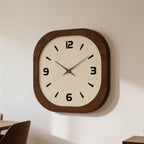Wood framed square clock seen at an angle on a plain wall above a dining chair