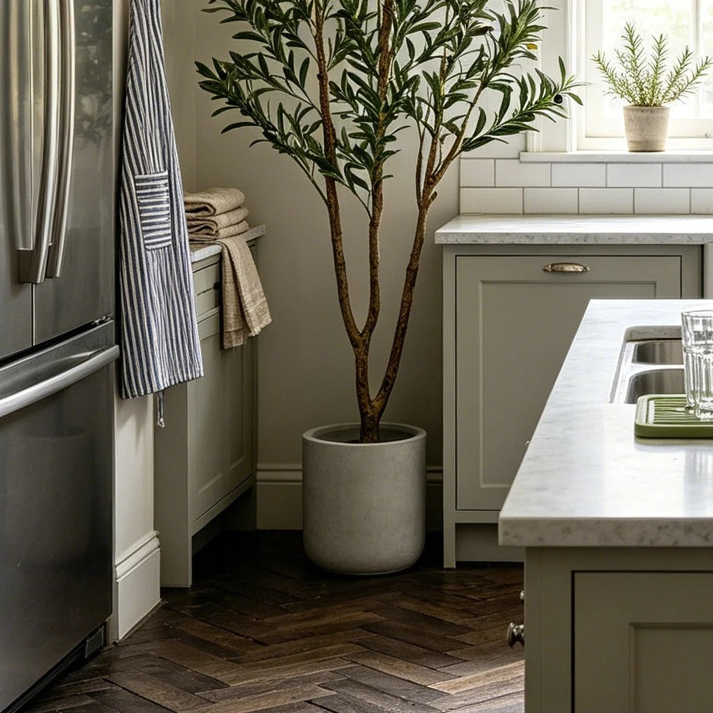 Artificial olive tree in a concrete planter beside a green kitchen island on herringbone flooring