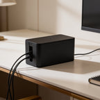 Black cord box at the corner of a pale desk with cables gathered at its left end
