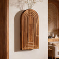 Carved arch wall vase with fine dried stems mounted beside an open doorway