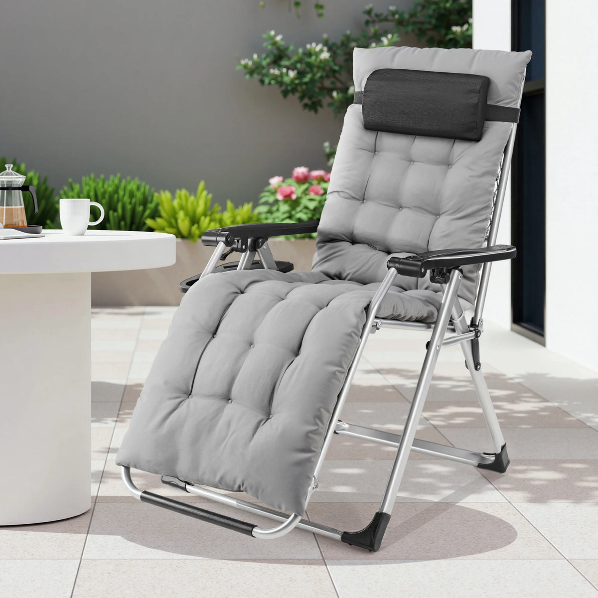 Light gray cushioned recliner on a patio next to a round white table and planters