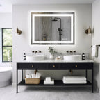 Lit mirror on a white wall above a black vanity, with a bathtub and window nearby