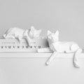 Pair of white geometric cats posed on a white ledge next to a book spine