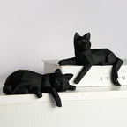 Black geometric cats, one seated on a book and one lying on a white ledge
