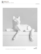 Single white faceted cat resting on a white ledge in a bordered layout panel
