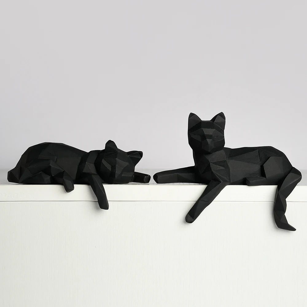 Two black faceted cats lying side by side along a white ledge