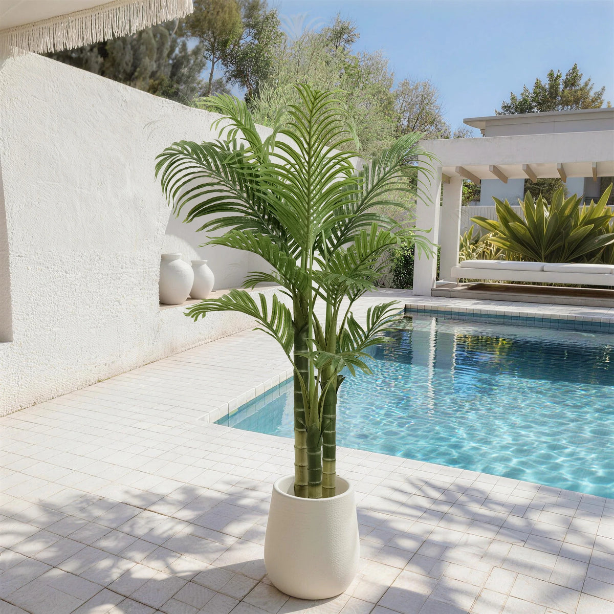 Artificial palm in a white planter on a poolside patio beside a white wall