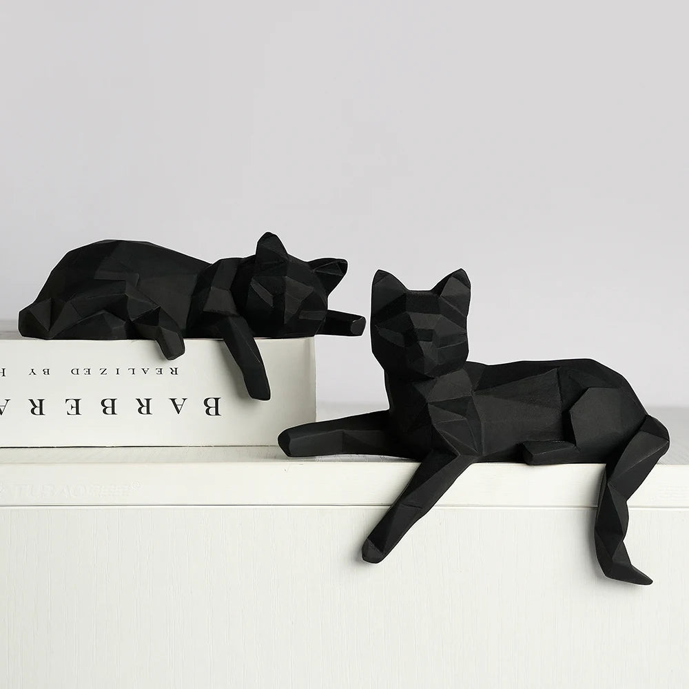 Two black faceted cat figures resting on a white ledge beside a book