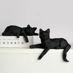 Two black faceted cat figures resting on a white ledge beside a book