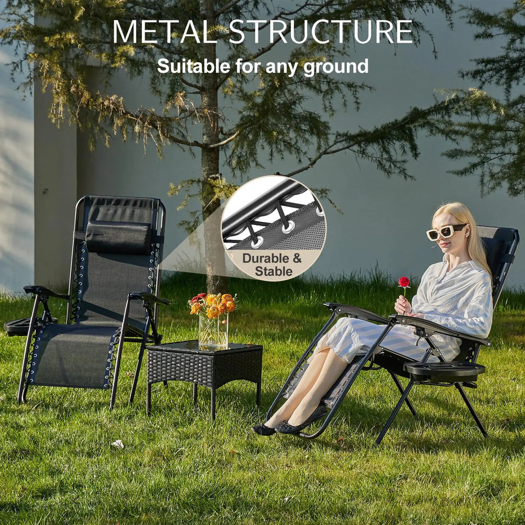 Two folding recliners set up on grass under a tree, one with a woman seated and reading