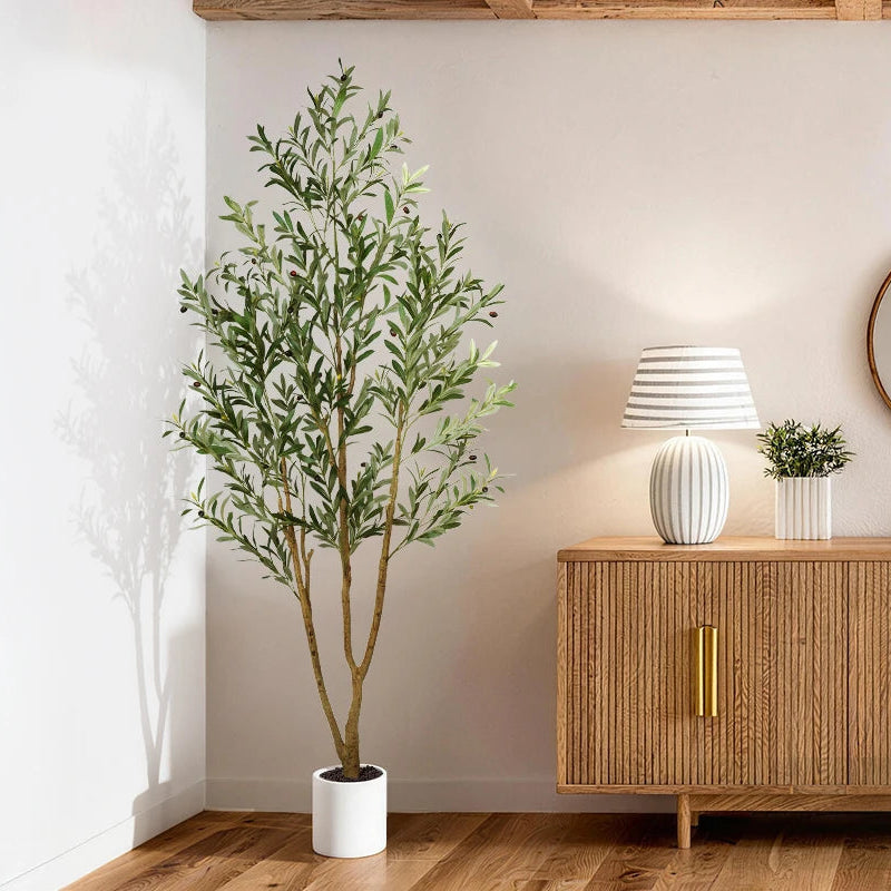 Artificial olive tree next to a wood sideboard holding a ribbed white lamp