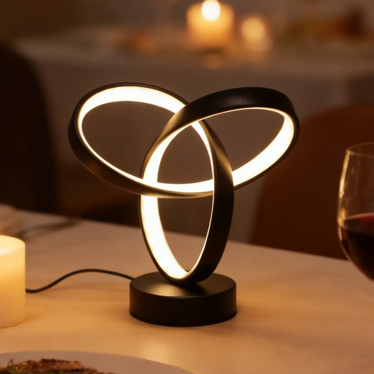Sculptural knot lamp glowing on a dining table next to a wine glass and candles