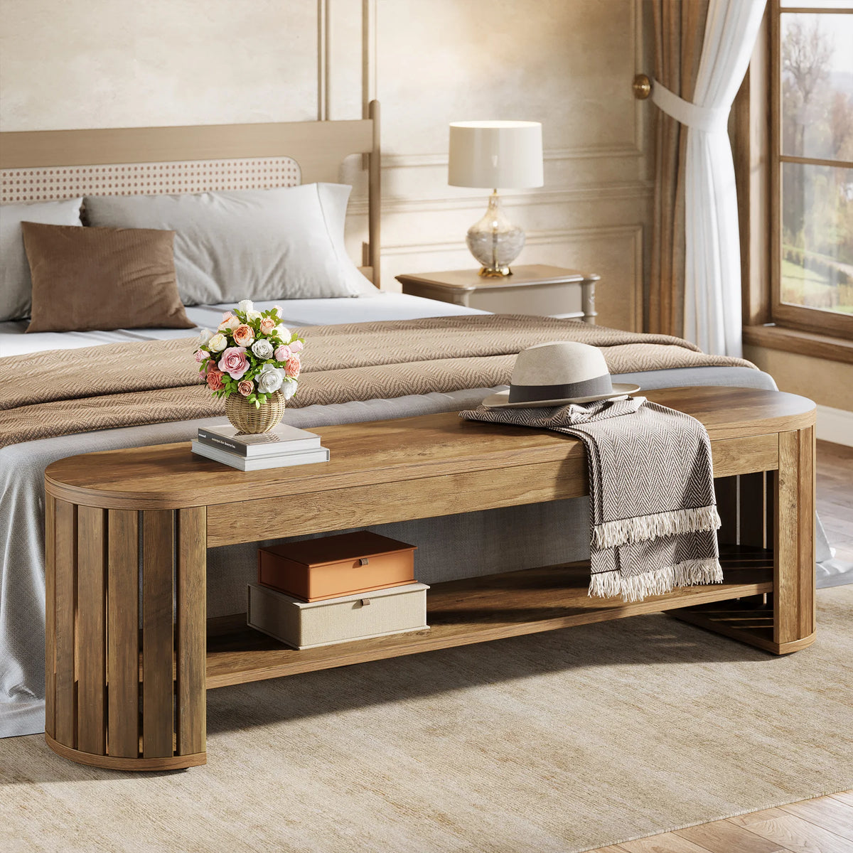 Wood bench at the foot of a bed with a box on its lower shelf and flowers on top
