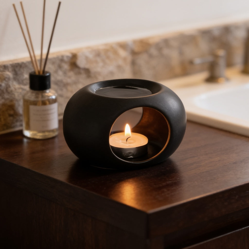 Close angle on the black pebble warmer, flame visible through its side opening on a bath counter