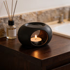 Close angle on the black pebble warmer, flame visible through its side opening on a bath counter