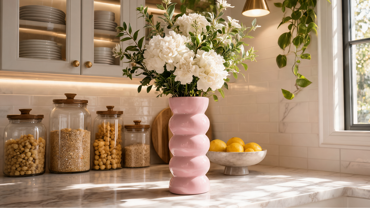Glossy pink glazed ceramic bubble vase holding white hydrangeas on a sunlit marble kitchen counter