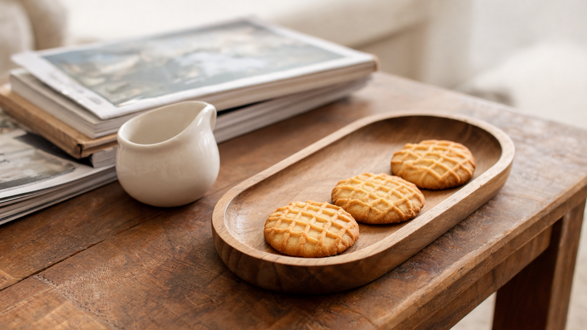 Long narrow solid wood serving tray holding biscuits and a small ceramic creamer on a dining table
