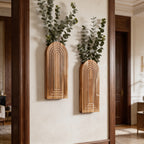 Two arched wood wall vases holding trailing eucalyptus on a cream wall
