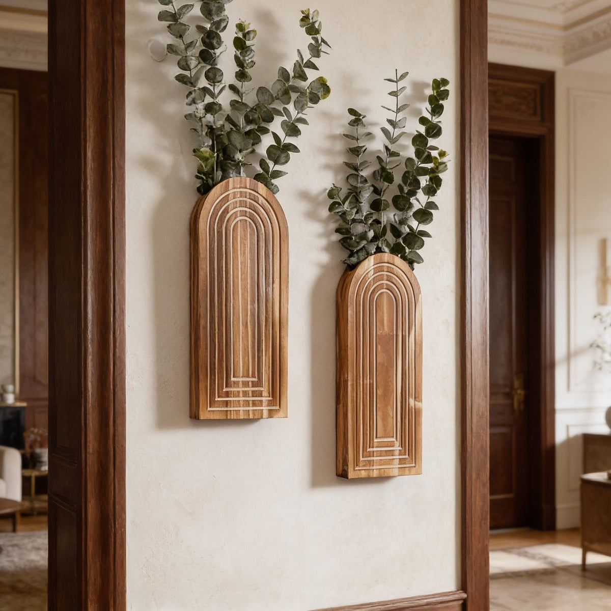 Two arched wood wall vases holding trailing eucalyptus on a cream wall