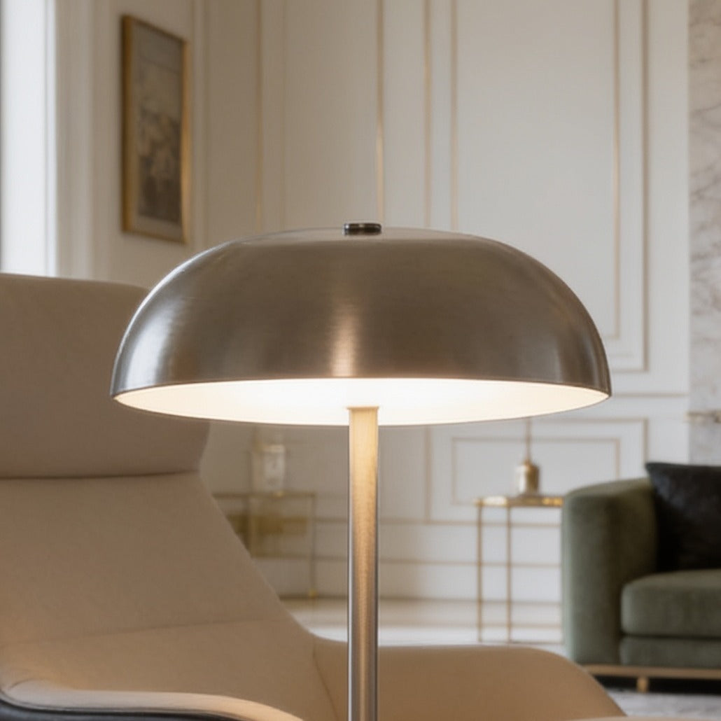 Brushed silver dome lamp lit on a table in a room with a green sofa