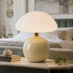 Glass dome lamp on a pale yellow base lit at the corner of a bedside table