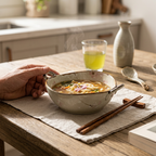 Noodle bowl and chopsticks on a wooden table with a glass of juice