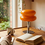 Amber glass lamp on a wood table by a window with a mug and an open book