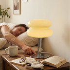Yellow glass lamp lit on a nightstand while someone sleeps in the bed behind