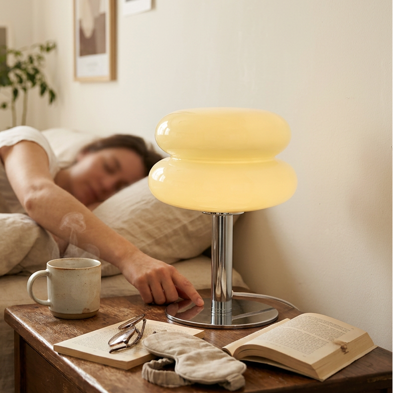 Yellow glass lamp lit on a nightstand while someone sleeps in the bed behind