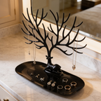 Black branching jewelry stand on an oval tray holding rings and necklaces