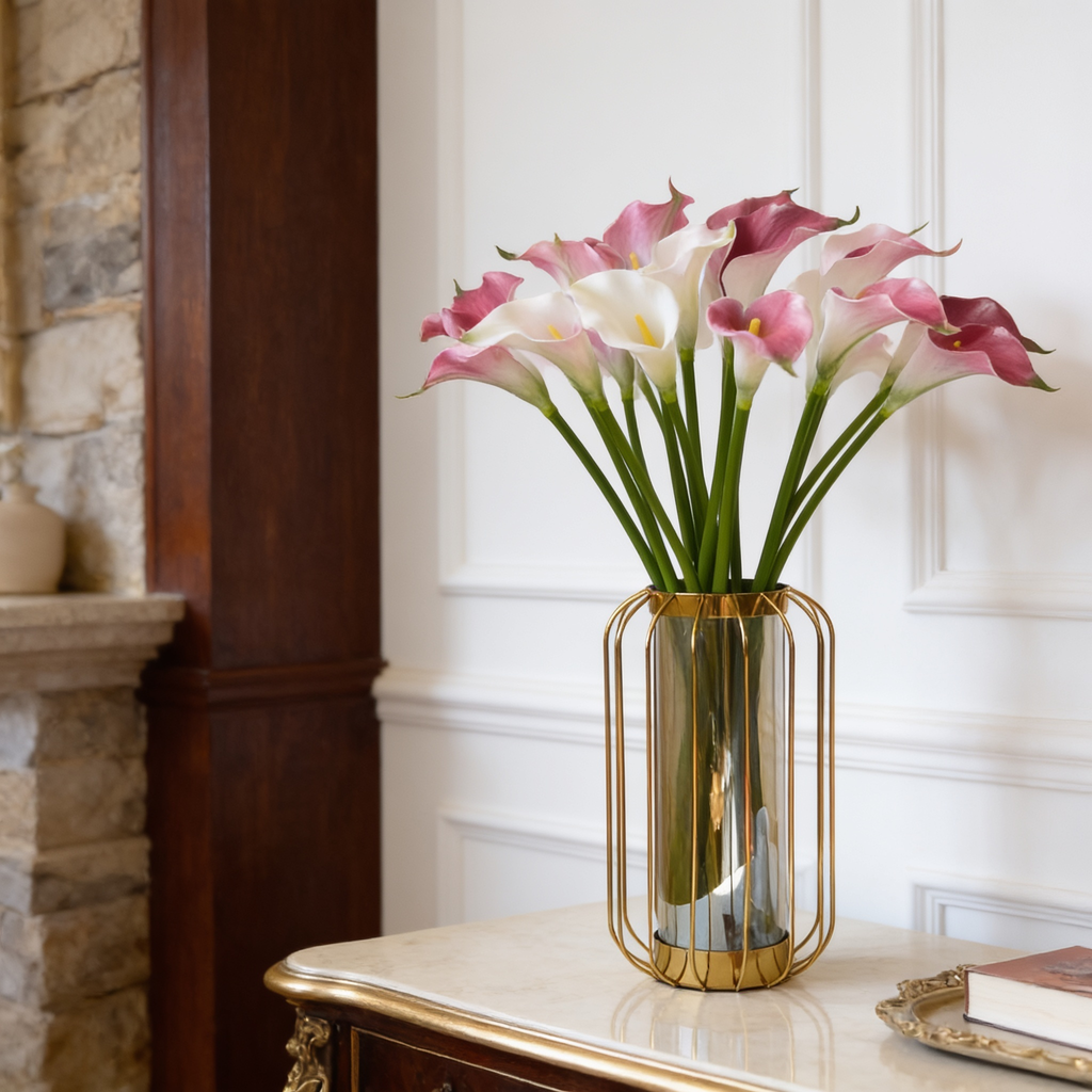 Pink and white calla lily stems in an amber glass vase by a stone fireplace