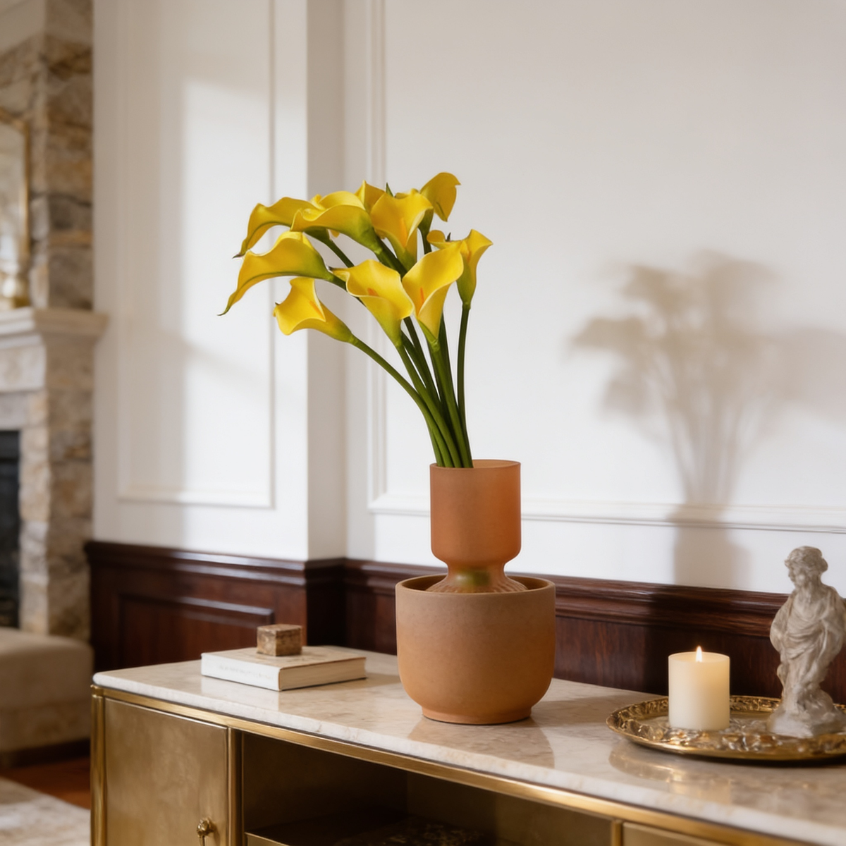 Yellow calla lilies in a terracotta vase on a console with a tray and candle