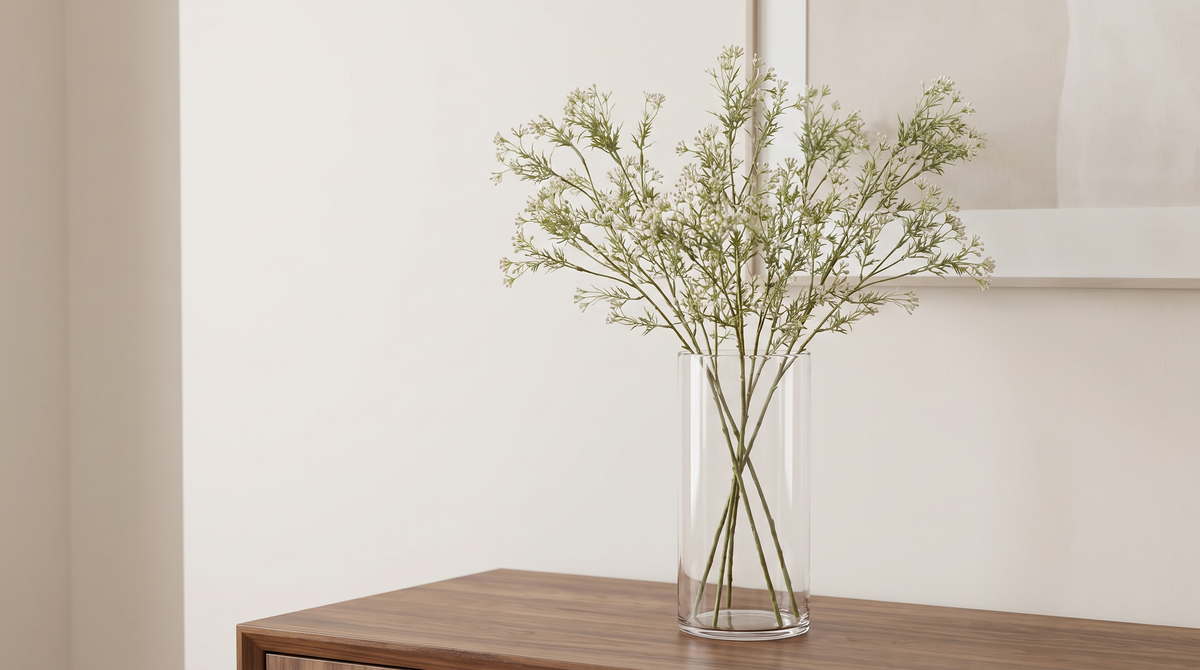 White faux gypsophila branches in a tall glass vase on a walnut console