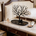 Black jewelry tree on a marble vanity next to a mirror and perfume bottle