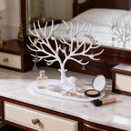 White branching jewelry tree on a vanity beside perfume bottles and a compact