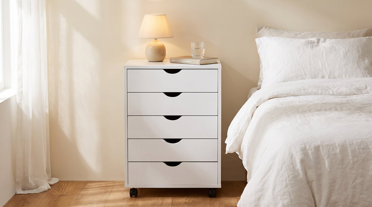 White five drawer rolling cabinet used as a nightstand beside a bed