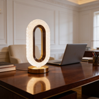 Glowing oval halo lamp on a gold base lighting a dark wood desk with books