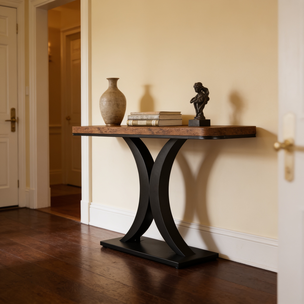 Hourglass base console against a warm wall with a vase, books and a small bust