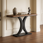 Narrow console with an hourglass black base and wood top styled with a vase and books