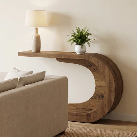 Sculptural wood console beside a cream sofa with a lamp and a small plant