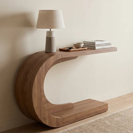 C shaped console table with a lamp and books against a plain white wall