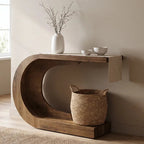 Curved C shaped wood console holding a white vase with a woven basket beneath
