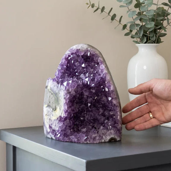 Amethyst cluster on a gray table with a hand alongside it and eucalyptus stems