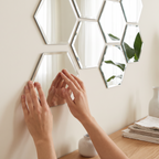 Hands pressing a hexagon mirror tile onto a white wall