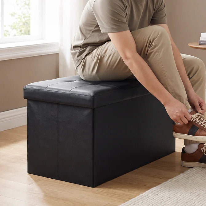 Person seated on the black bench tying a shoe on a wood floor