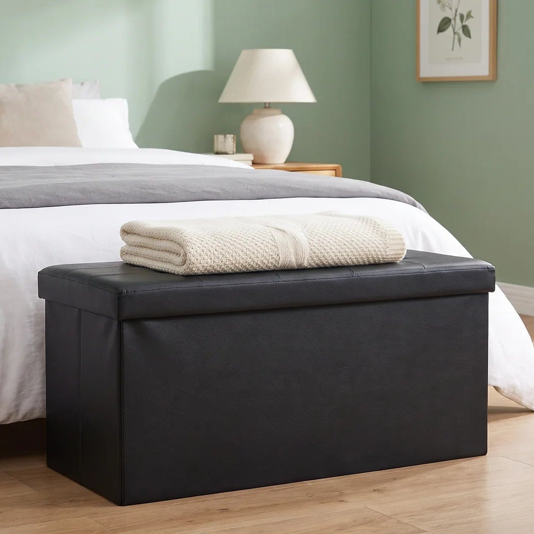 Black bench holding folded towels at the foot of a bed by a green wall