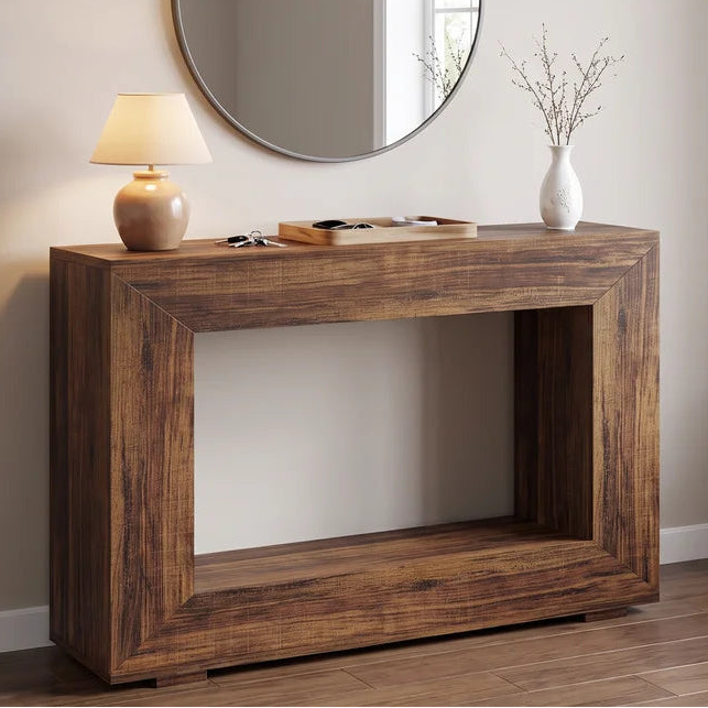 Wood console below a round mirror with a lit lamp and dried stems