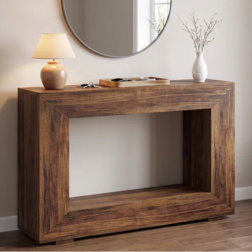 Wood console below a round mirror with a lit lamp and dried stems