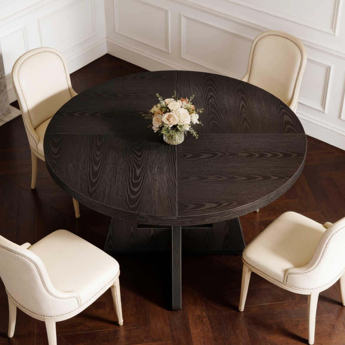 Black round dining table with cream chairs and a small vase of flowers